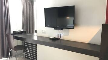 A modern room with a flat-screen TV mounted on a dark counter, a chair, and a small table with a remote control.