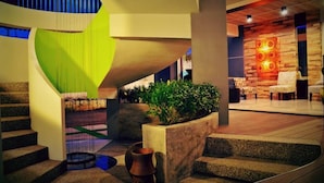 Un interior moderno con escalera, un muro verde decorativo y una zona de estar con revestimiento de madera y una lámpara ornamental.