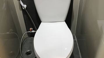 A white toilet with a tank and a bidet attachment in a bathroom with dark tiled walls and floor.