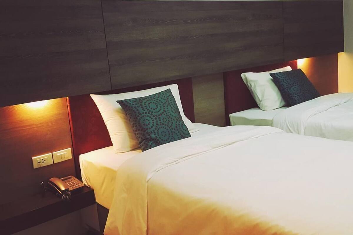 A hotel room with two beds, a bedside telephone, and a wall-mounted light fixture.