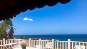 Un balcón con sillas y una mesa blancos, con vistas a la costa, el océano y el litoral rocoso.