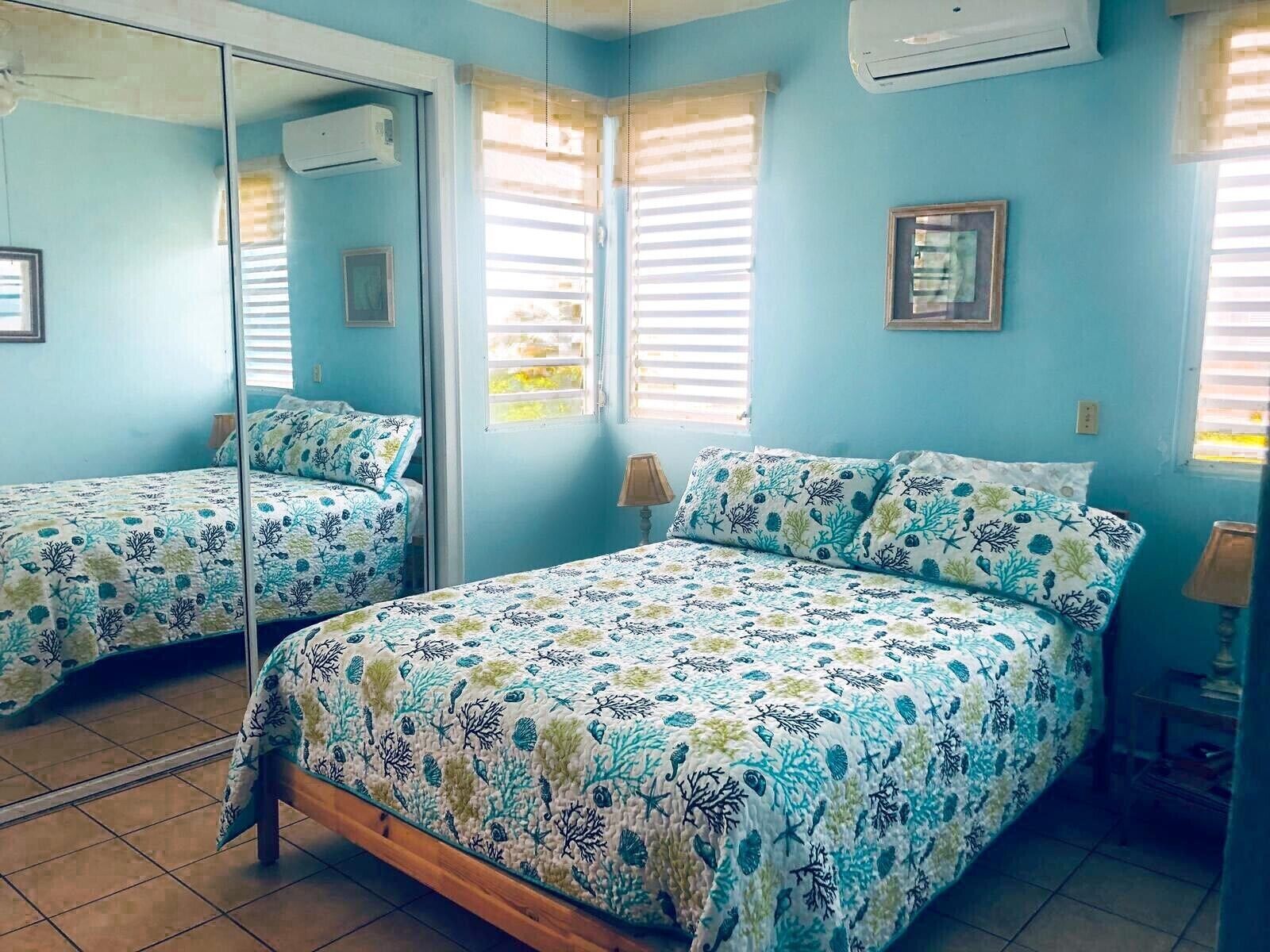A bedroom with two beds, a large mirror, and a window with blinds.