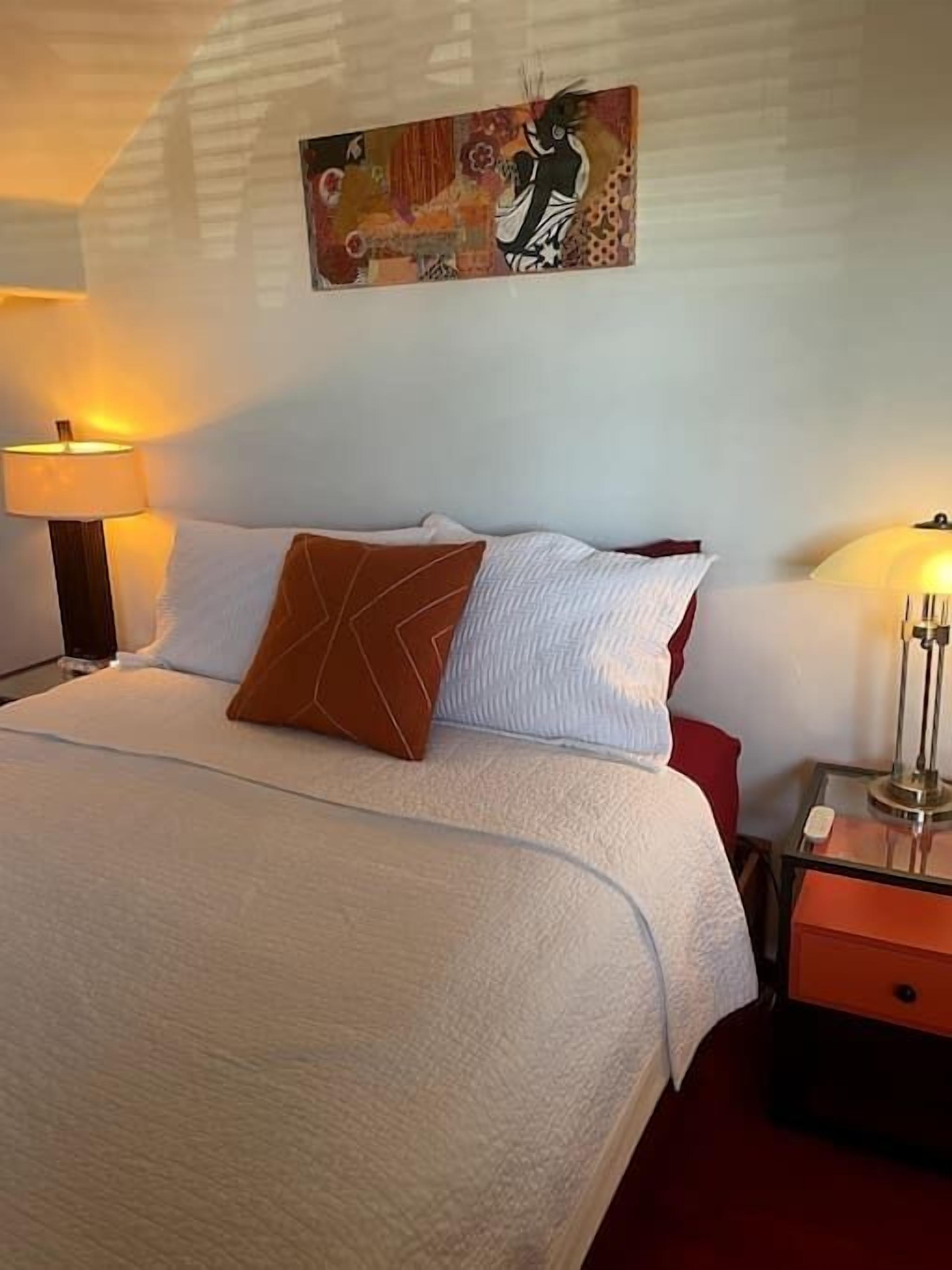 A neatly made bed with white and brown pillows, a decorative wall piece, and two bedside lamps.