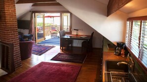A cozy loft-style room with a dining area, a kitchen with a sink, and a view through a large window.