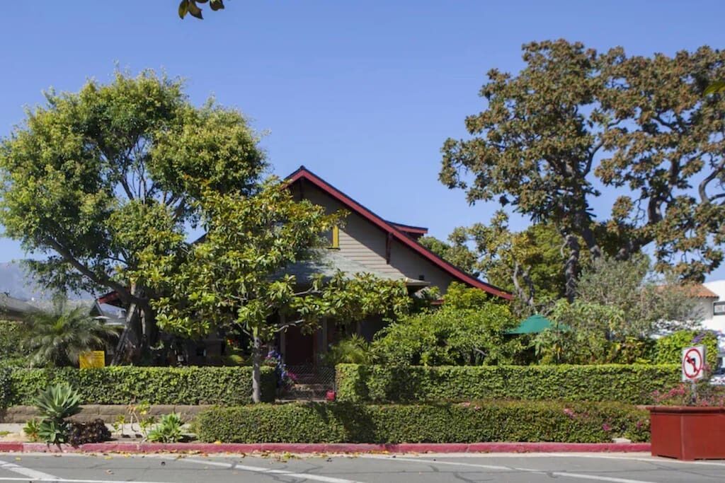 A house with a red roof, surrounded by lush greenery and a well-maintained hedge.