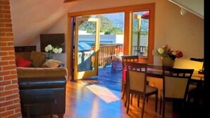 A cozy loft-style room with a wooden floor, a dining area with a table and chairs, and a large sliding glass door leading to a balcony.