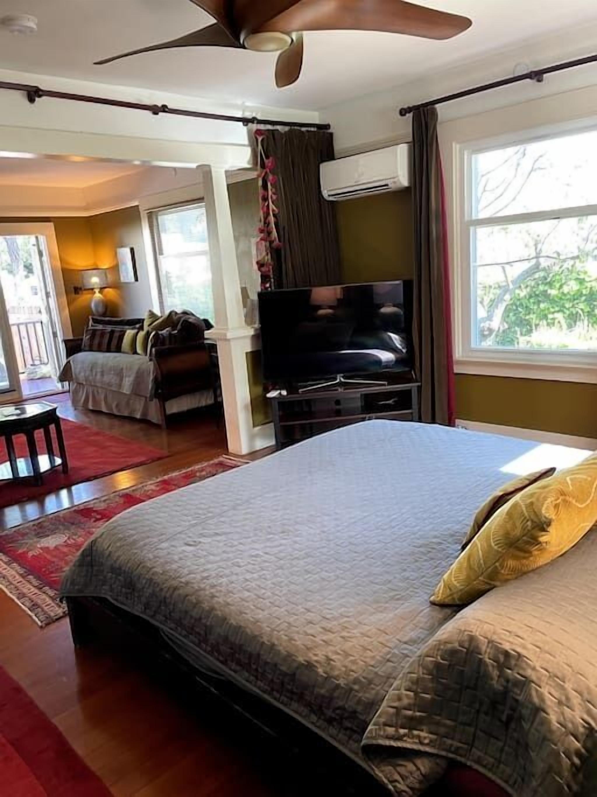 A bedroom with a bed, a TV, a ceiling fan, and a window.