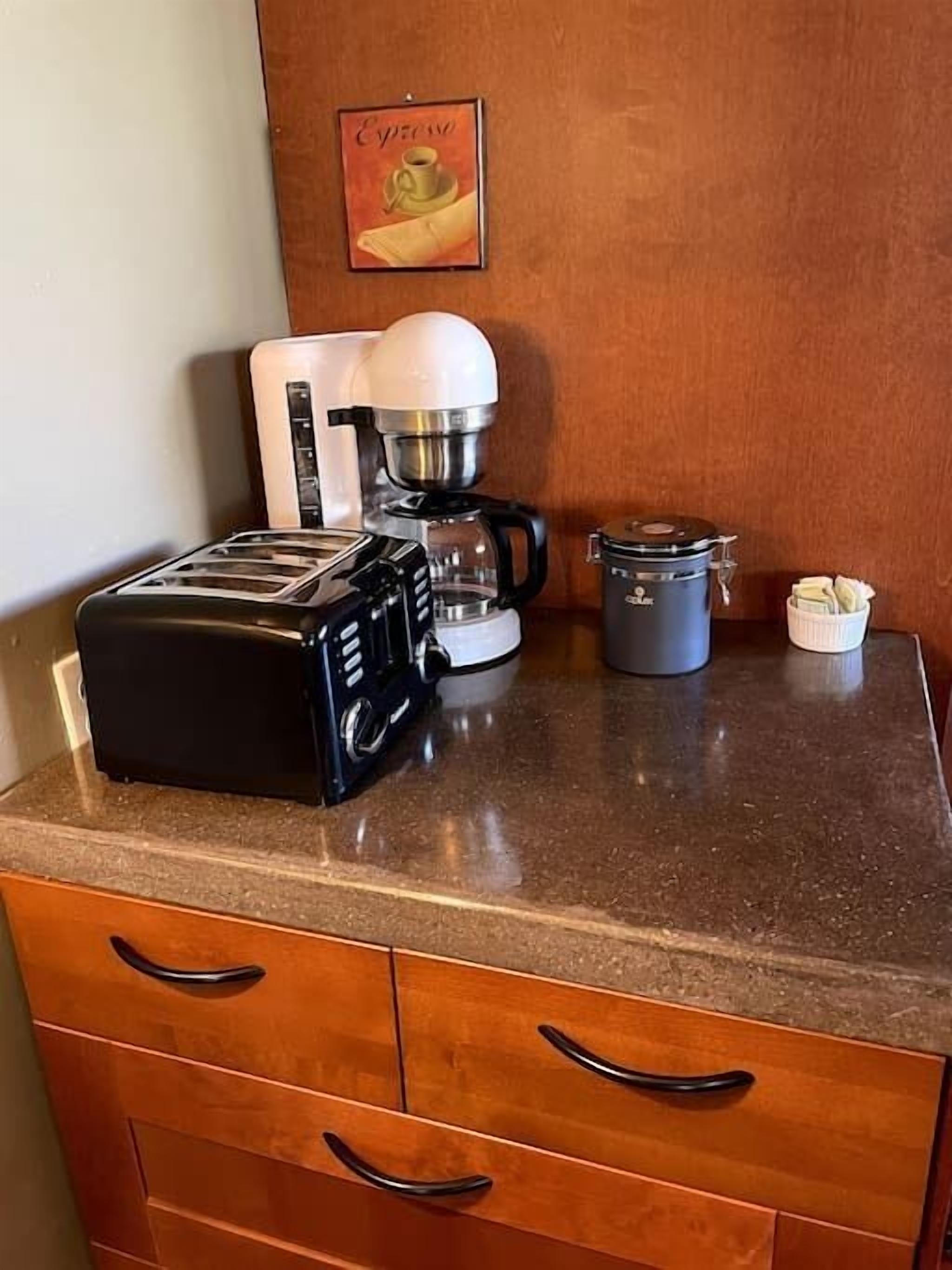A kitchenette with a toaster, coffee maker, and a small container on the countertop.