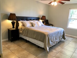 A bedroom with a bed, two nightstands with lamps, a ceiling fan, and a window.