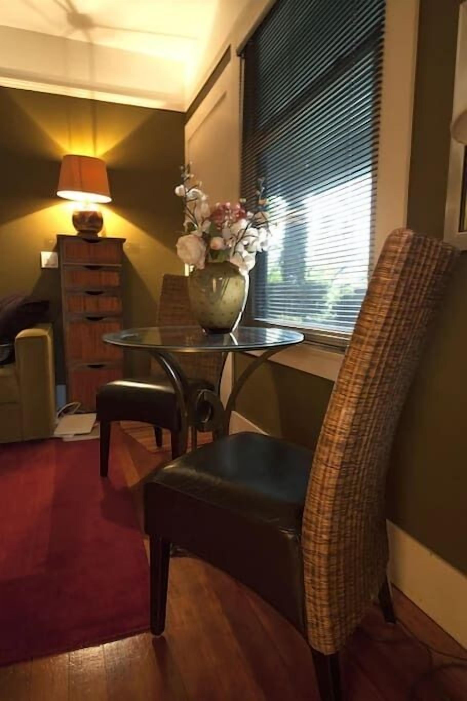 Een gezellige kamer met een eettafel, stoelen, een lamp en een vaas met bloemen.