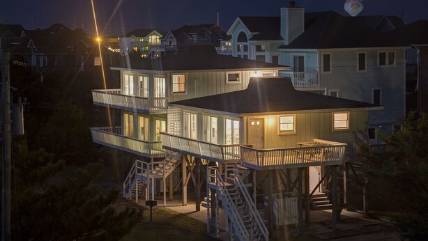 A multi-level house with external staircases and balconies, surrounded by other houses.