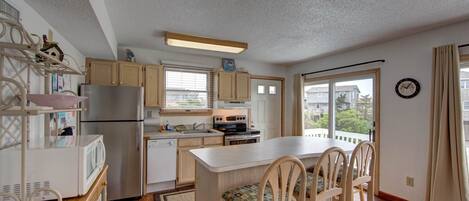A compact kitchen with a refrigerator, stove, microwave, and wooden cabinets. There is a dining area with a table and chairs, and a large window providing a view of the outside.