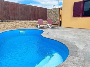 A swimming pool with a stone wall and a wooden fence in the background.