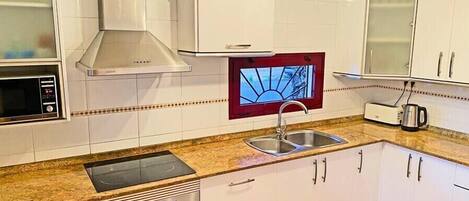 A modern kitchen with white cabinets, a stainless steel sink, a built-in oven, a microwave, and a red-framed window.