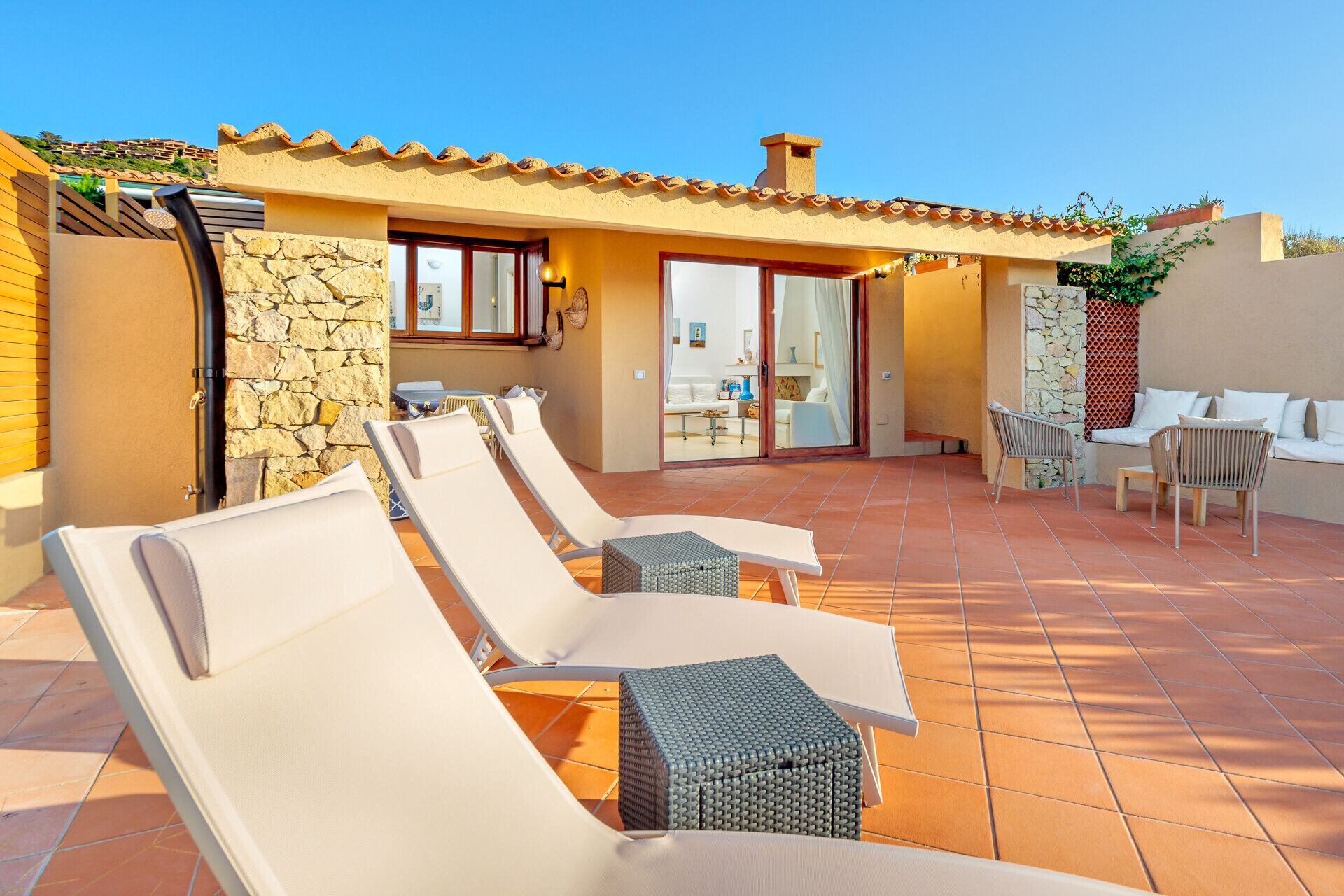 A sunlit outdoor patio with lounge chairs and a stone wall.