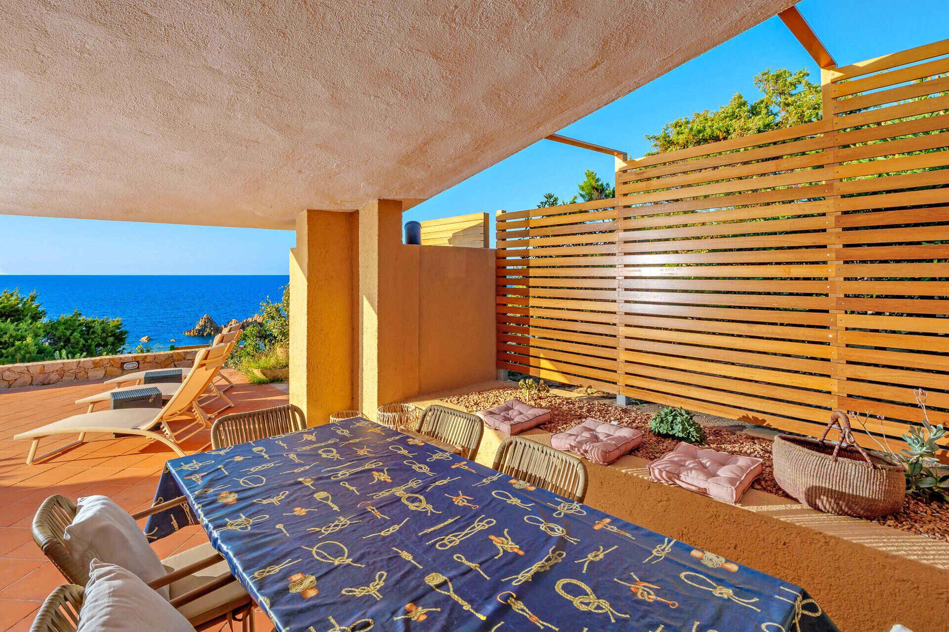 Una terraza con mesa lista para comer, asientos exteriores y vistas al mar.