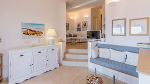 Una sala de estar bien iluminada con un mueble blanco, un sofá azul y un televisor sobre un soporte.