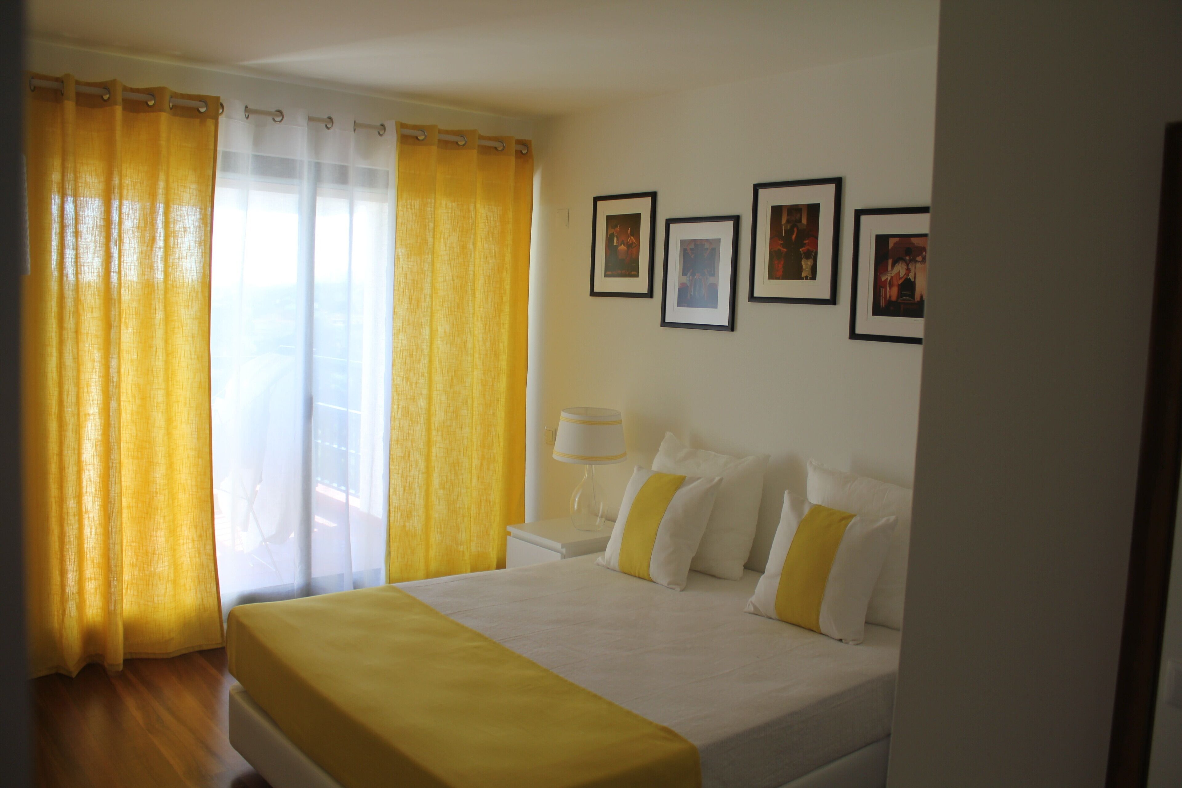 A hotel room with a bed, curtains, a nightstand, and framed pictures on the wall.