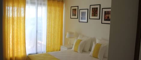 A hotel room with a bed, curtains, a nightstand, and framed pictures on the wall.
