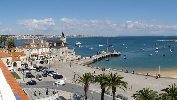 A coastal town with a sandy beach, a marina with boats, and buildings along the waterfront.