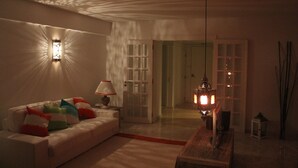 A living room with a white sofa, colorful cushions, a lamp, and a decorative hanging light fixture.