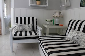 A room with a striped chair and bed, a small table with a lamp, and a basket on a shelf.