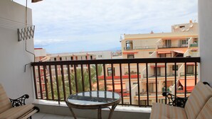 A balcony with a glass table and two striped sofas, overlooking a residential area with buildings and a clear sky. - Comfortable and nice apartment in Beachfront in Los Cristianos (Playa de Los Cristianos, Arona)