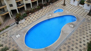 A large swimming pool with a tiled deck, surrounded by a multi-story building with balconies and a small garden area. - Comfortable and nice apartment in Beachfront in Los Cristianos (Playa de Los Cristianos, Arona)