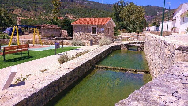 A stone-walled pool with a clear water surface, surrounded by a paved walkway and a small stone building with a red-tiled roof. - Holiday Cottage in the Natural Park  (Alcobertas)