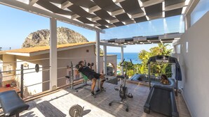 Une salle de sport située sur le toit, équipée de matériel d’exercice, avec un banc et une vue sur l’océan.
