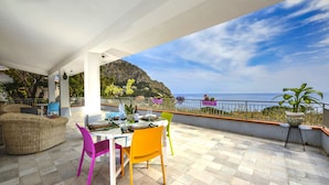 Une terrasse aménagée avec un coin repas, un canapé en osier et une vue sur la mer et les montagnes.