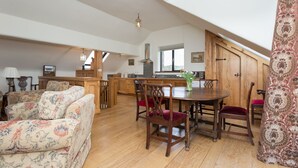 A spacious loft with a high ceiling, wooden dining table, and a cozy seating area with patterned sofas. - Traditional & spacious 2 bedroom cottage on the edge of the Lake District  (Selside, Kendal, Cumbria)