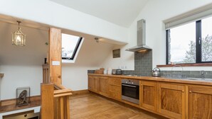 A modern kitchen with wooden cabinets, a built-in oven, and a large window providing natural light. - Traditional & spacious 2 bedroom cottage on the edge of the Lake District  (Selside, Kendal, Cumbria)