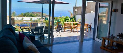 A living room with a sofa, a table, and a view of the patio area with a table and chairs.