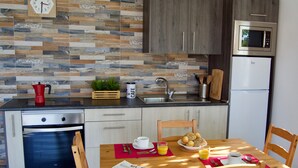 Una cucina moderna con forno integrato, microonde e frigorifero. C'è un tavolo da pranzo in legno con sedie, un sottopiatti rosso e un giornale. Sul bancone si trovano una macchina da caffè e una pianta.