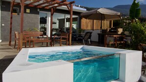 Una piscina con una pergola in legno e mobili da esterno, circondata da un patio con vista sulle montagne.