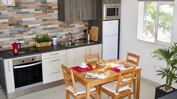 A modern kitchen with a wooden dining table, chairs, and a window with a view of greenery.
