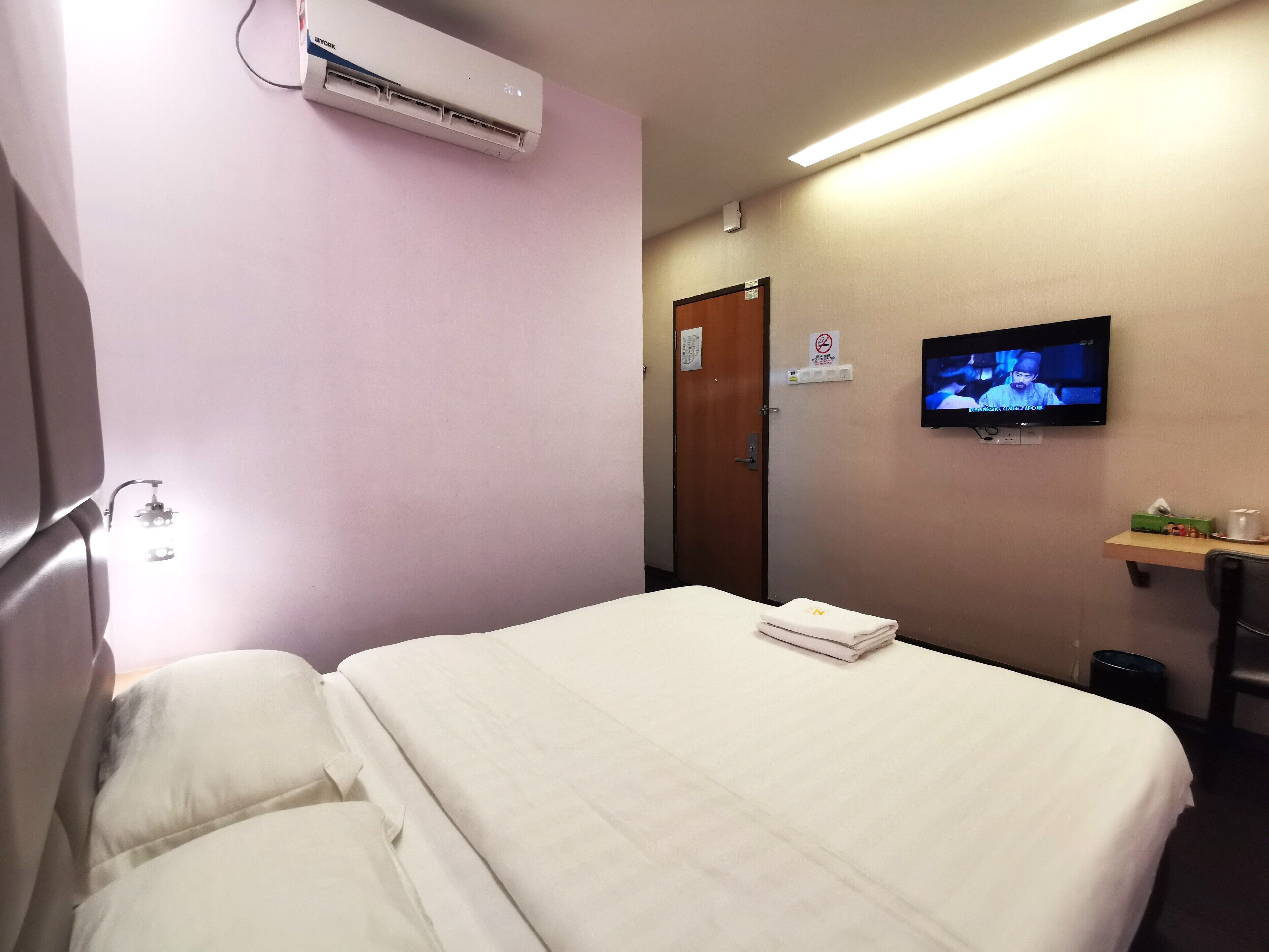 Ein Hotelzimmer mit Bett, Klimaanlage, Fernseher und einem kleinen Tisch mit Tasse und Schachtel.