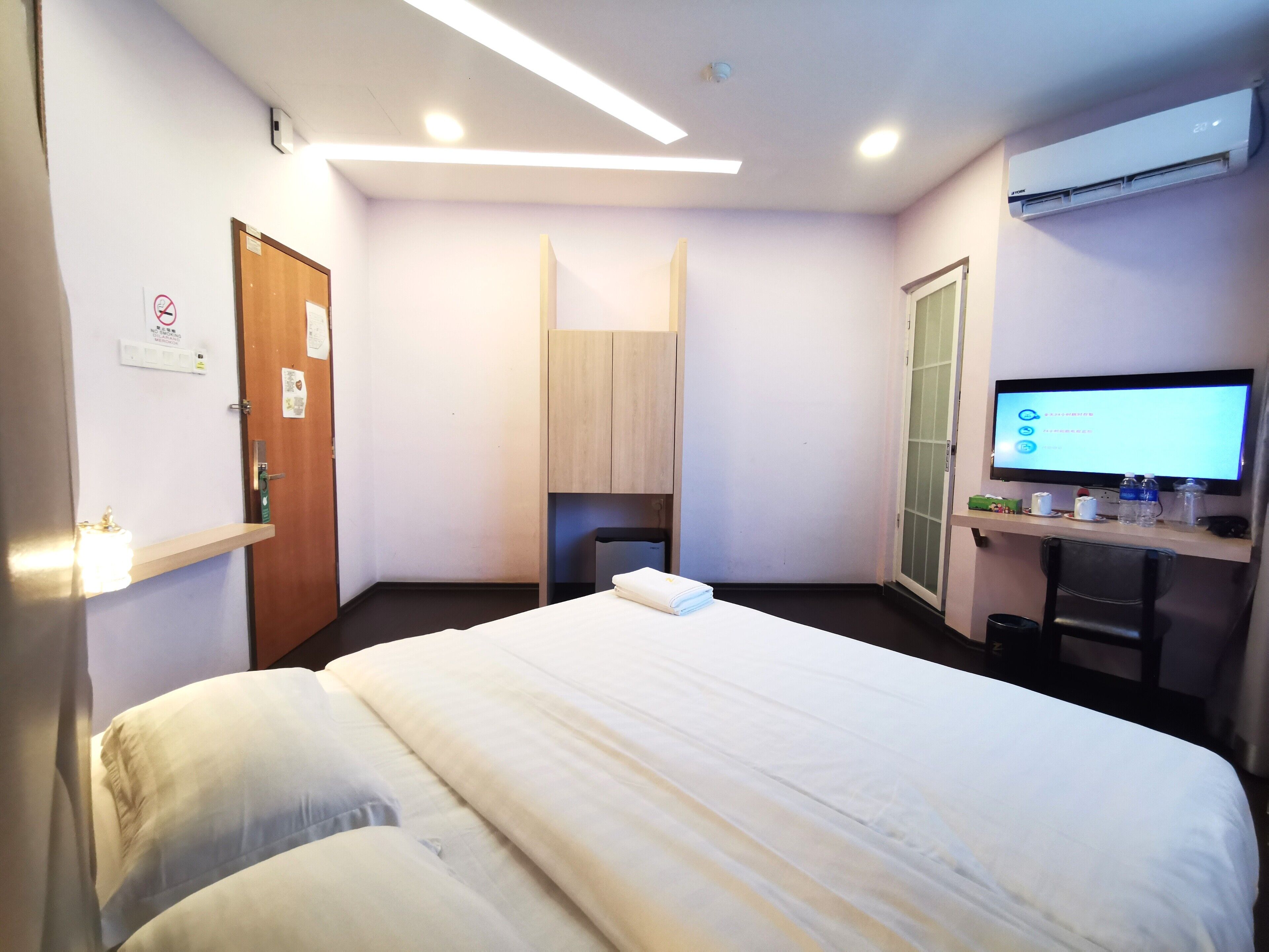 Una habitación de hotel con una cama, un escritorio con una computadora, un espejo y una puerta.