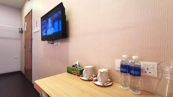 Habitación de hotel con un mostrador de madera, un televisor montado en la pared y dos botellas de agua sobre el mostrador.