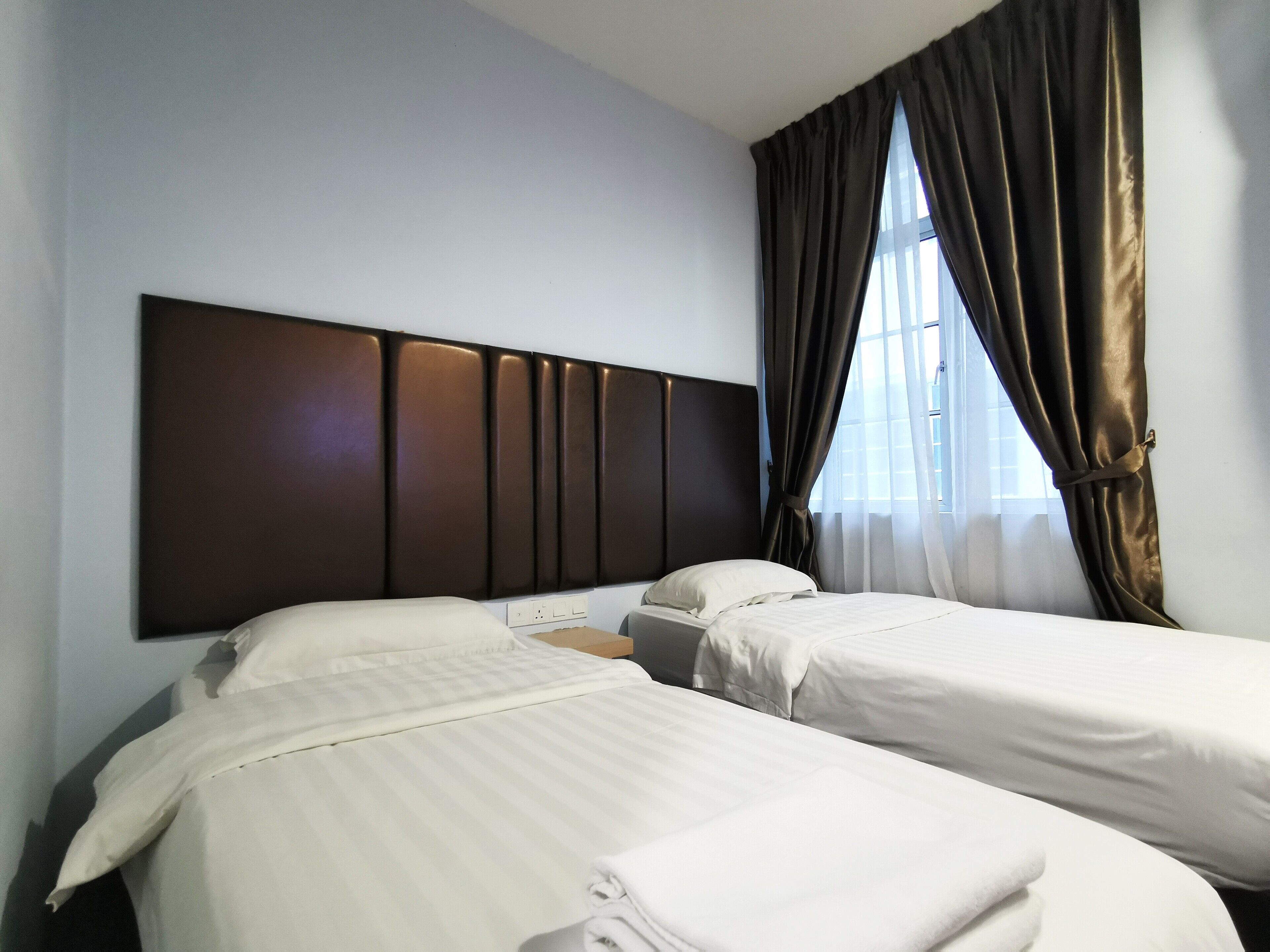 A hotel room with two beds, a dark headboard, and a window with curtains.
