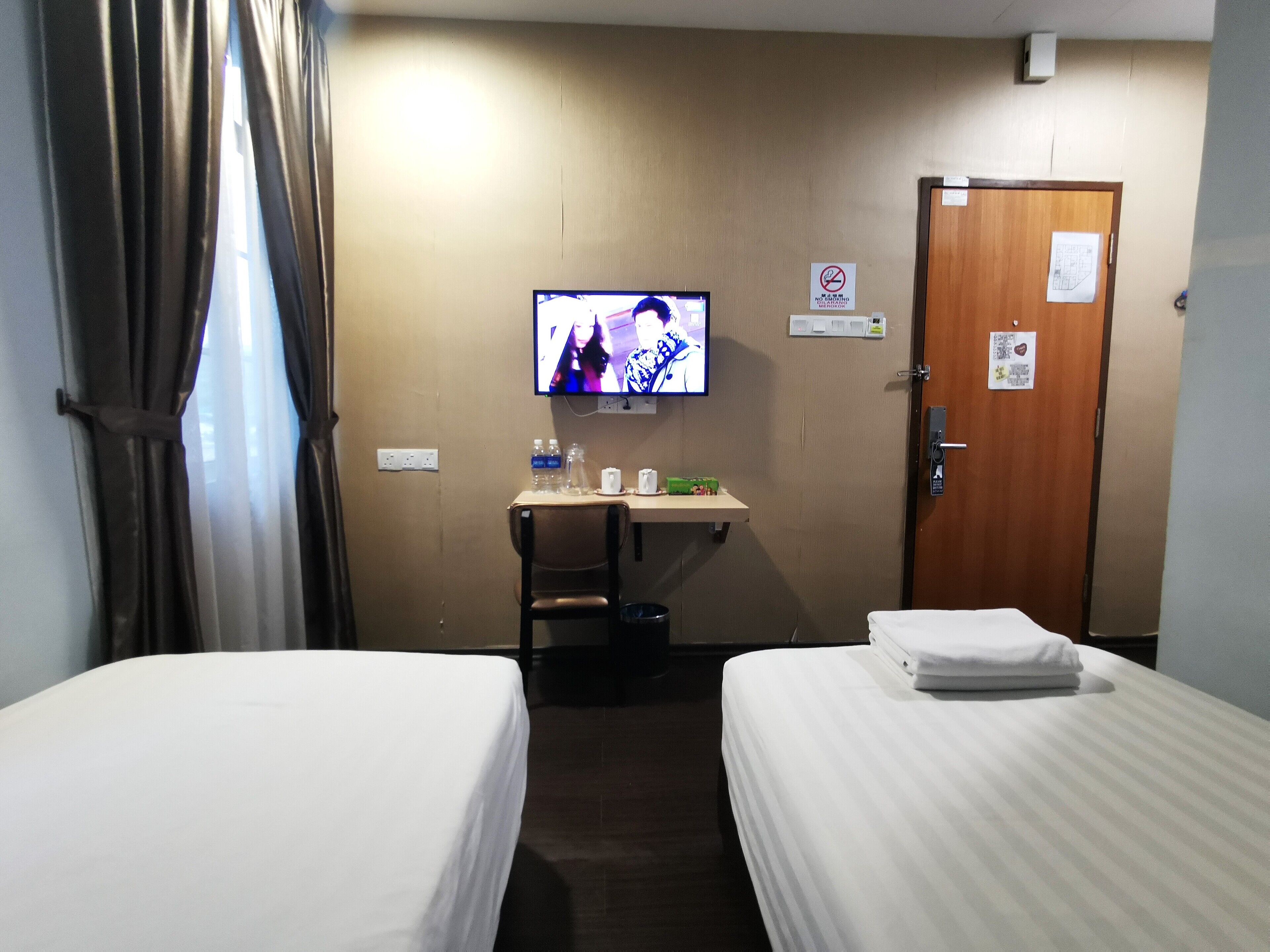 Una habitación de hotel con dos camas, un escritorio con televisor, una silla y una puerta.