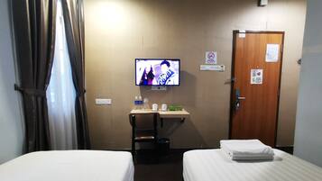 Una habitación de hotel con dos camas, un escritorio con televisor, una silla y una puerta.
