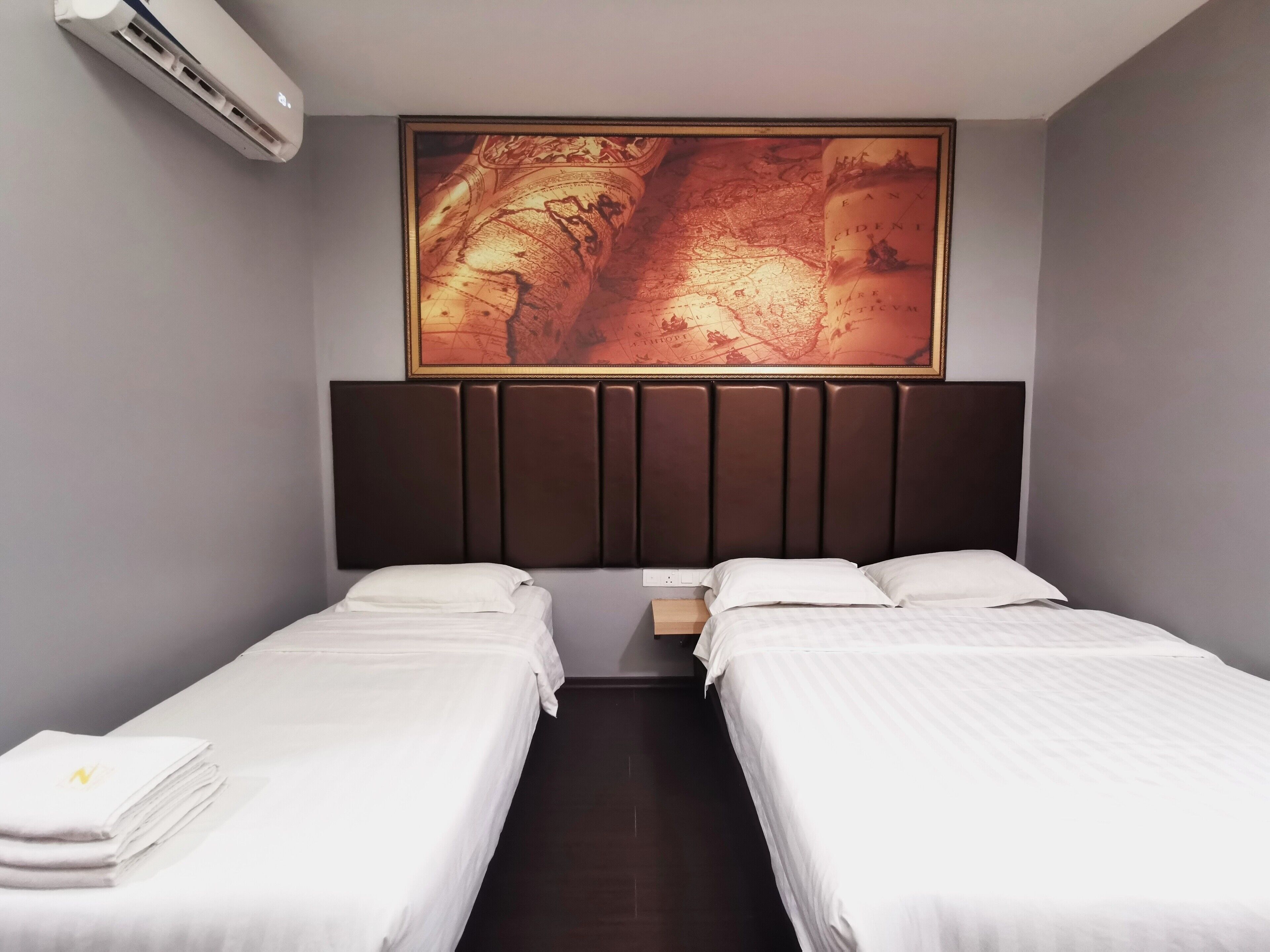 A hotel room with two single beds, a large framed map on the wall, a modern headboard, and a small bedside table.