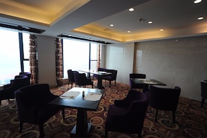 A hotel dining area with tables and chairs, large windows, and a patterned carpet.