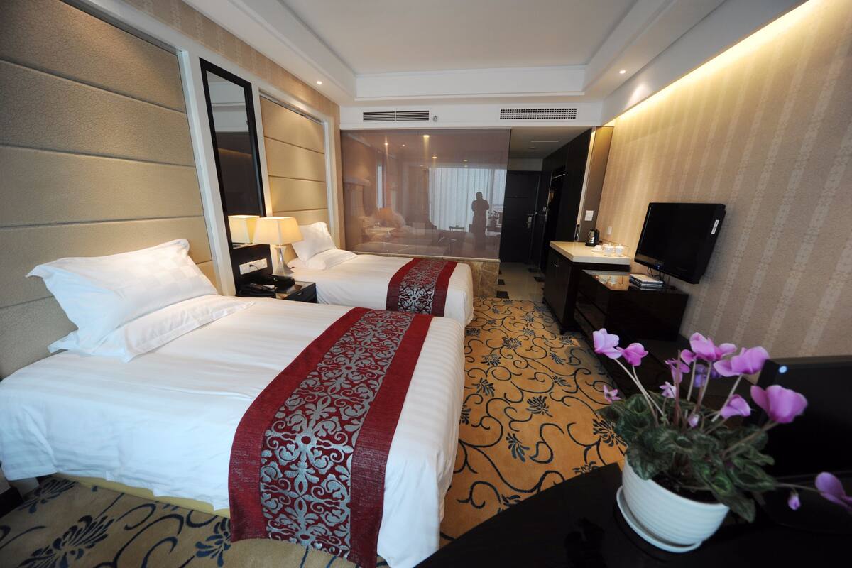 A hotel room with two beds, a TV, a desk, and a potted plant.