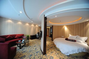 A hotel room with a curved ceiling, a bed with white linens, a red sofa, a small table with a plant, and a patterned carpet.