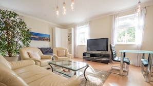 Ett vardagsrum med beige lädersoffor, ett soffbord i glas, en tv och en matplats med ett bord i glas och stolar i metall.
