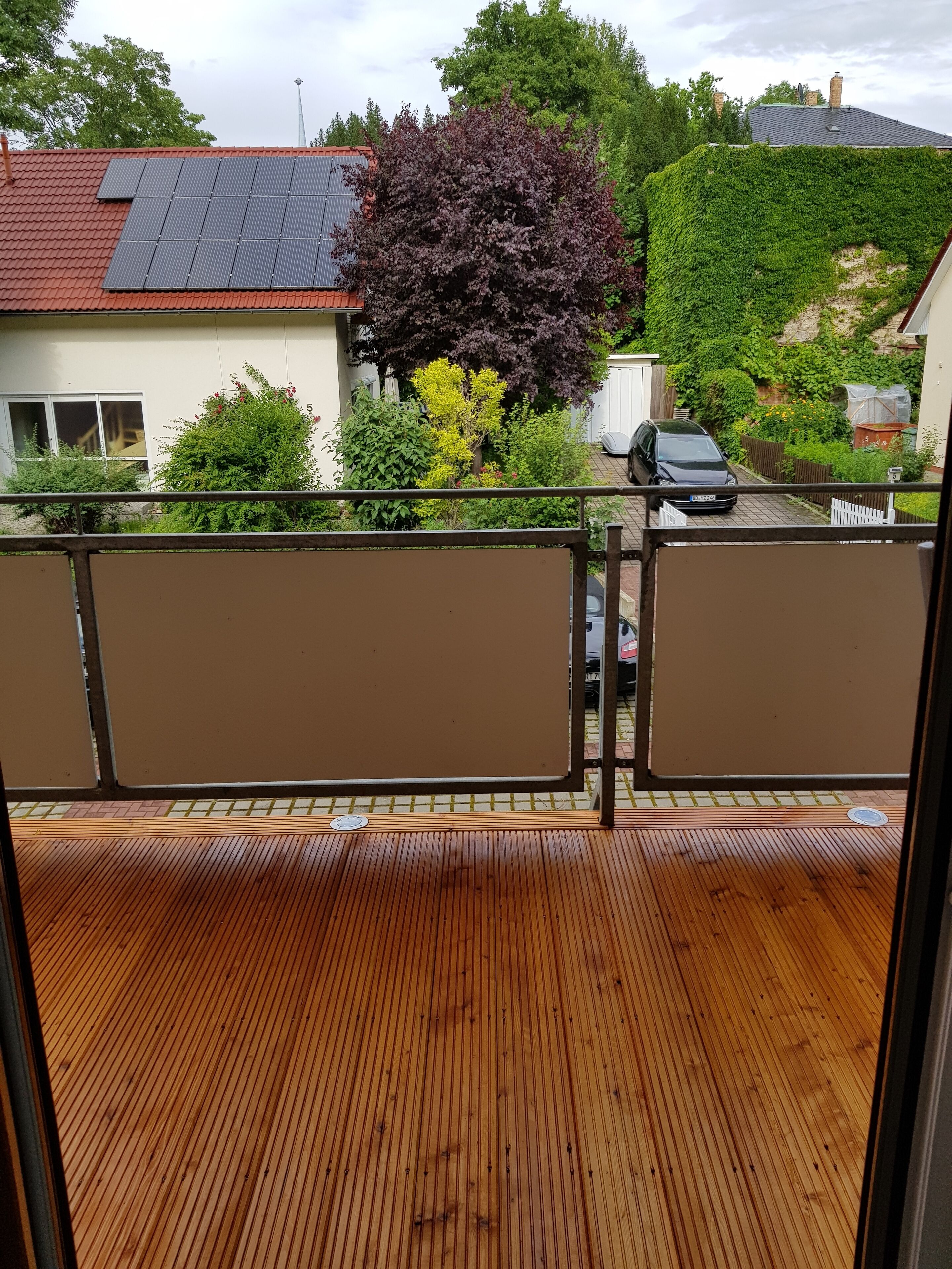 Eine Holzterrasse mit Blick auf eine Wohngegend, inklusive Häuser, eines Baumes und einem geparkten Auto.