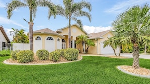 A residential house with a well-maintained lawn, palm trees, and a gated driveway. - Dream villa with tropical garden on the canal (Cape Coral)